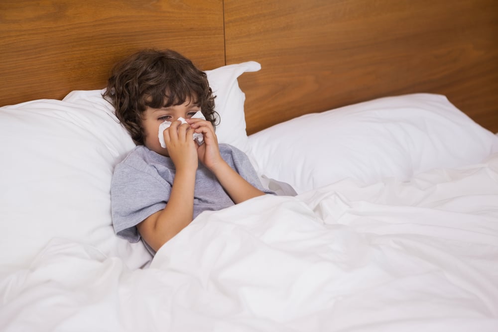 High angle view of a cute little boy suffering from cold as he lies in bed