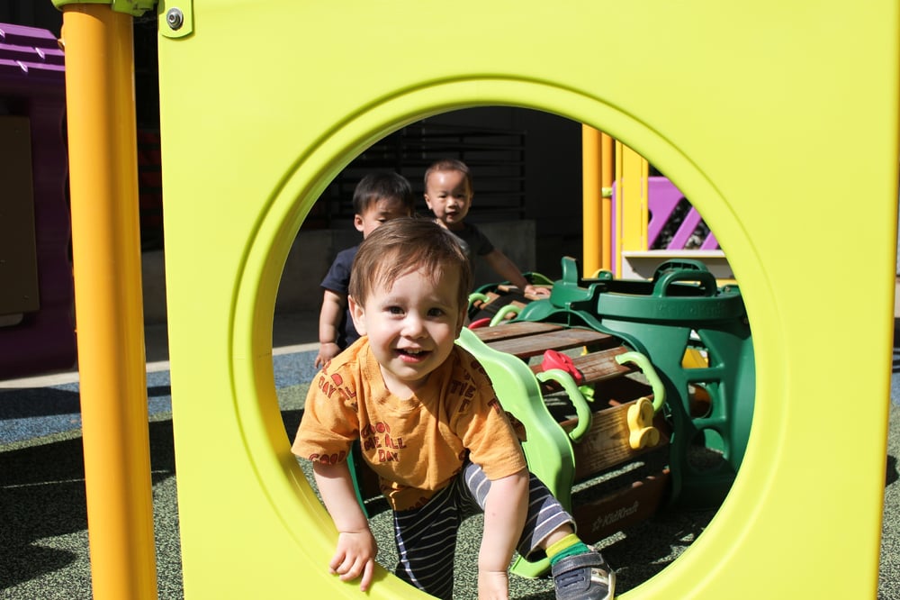 Young boy climbs through circular hole in jungle gym at a redwood city preschool